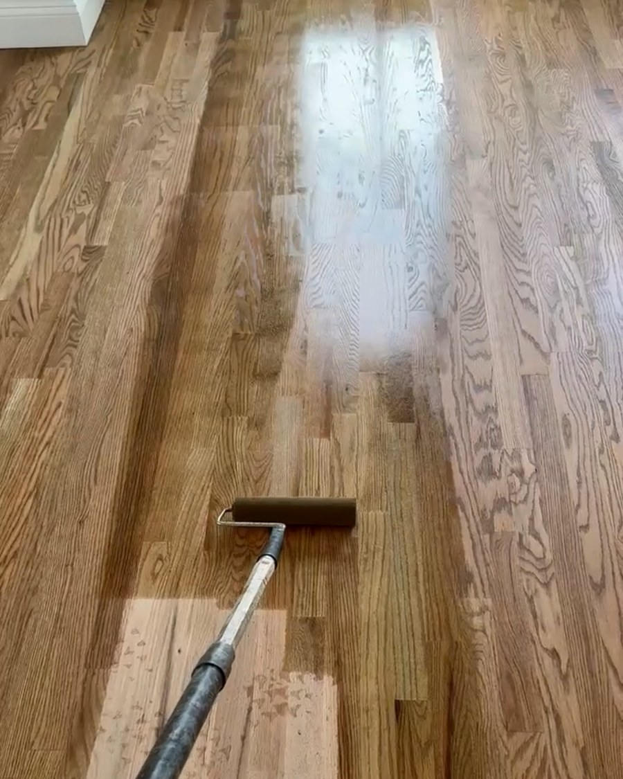 A protective finish coat being rolled onto a hardwood floor.