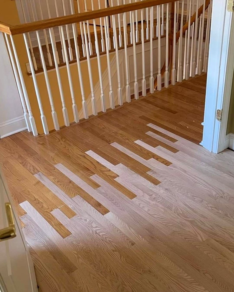 A repaired herringbone patch blended into an existing hardwood floor near a staircase.
