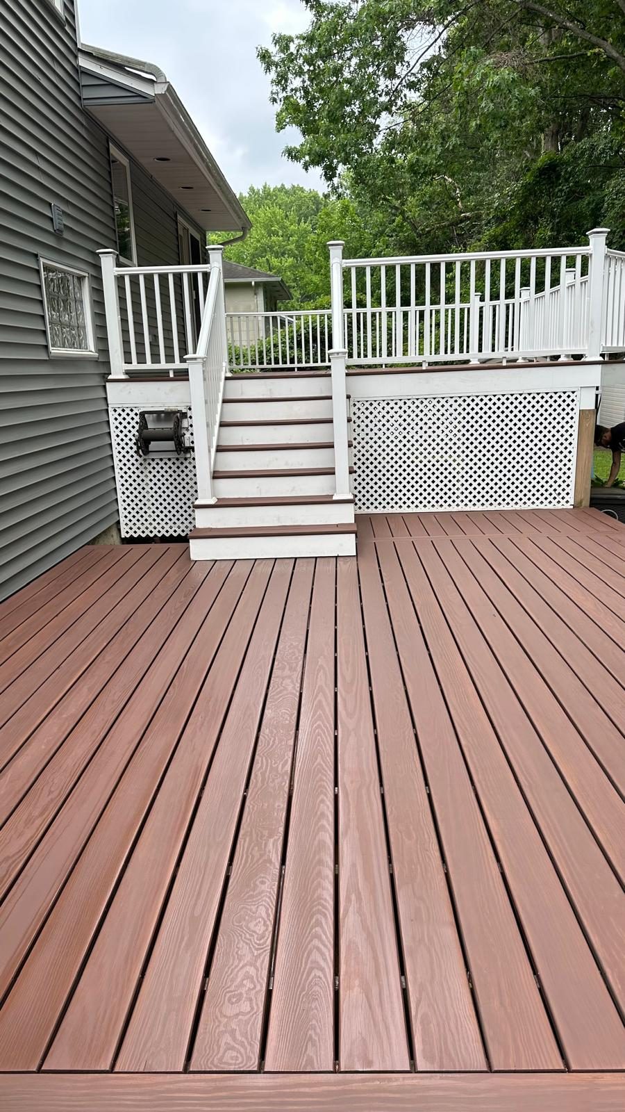 A stained composite deck with white railings and a staircase down to the yard.