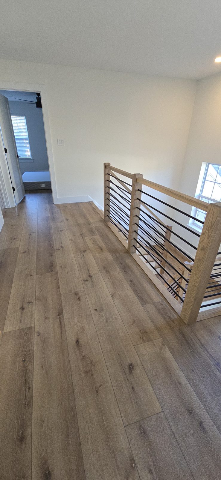New hardwood flooring on an upstairs landing, paired with a modern black cable railing.