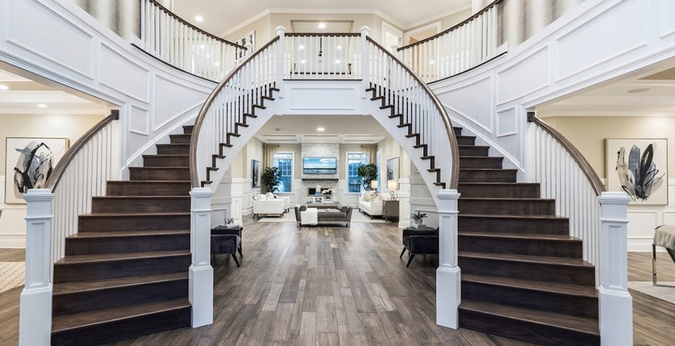 A grand two-story foyer with dual curved staircases and rich stained wood treads.