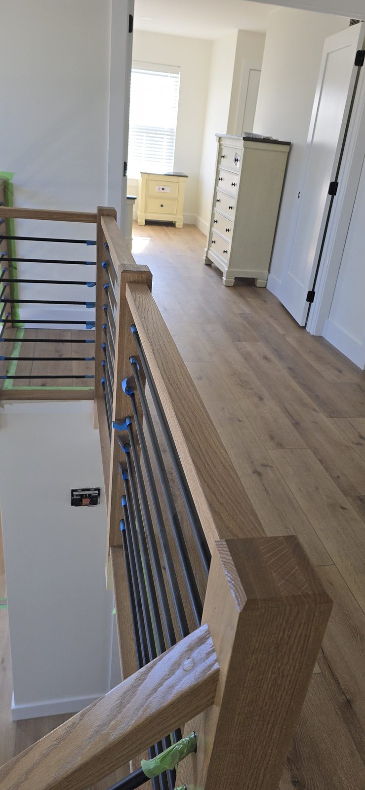 An upstairs landing mid-refinish, with cable railing taped off and furniture in place.