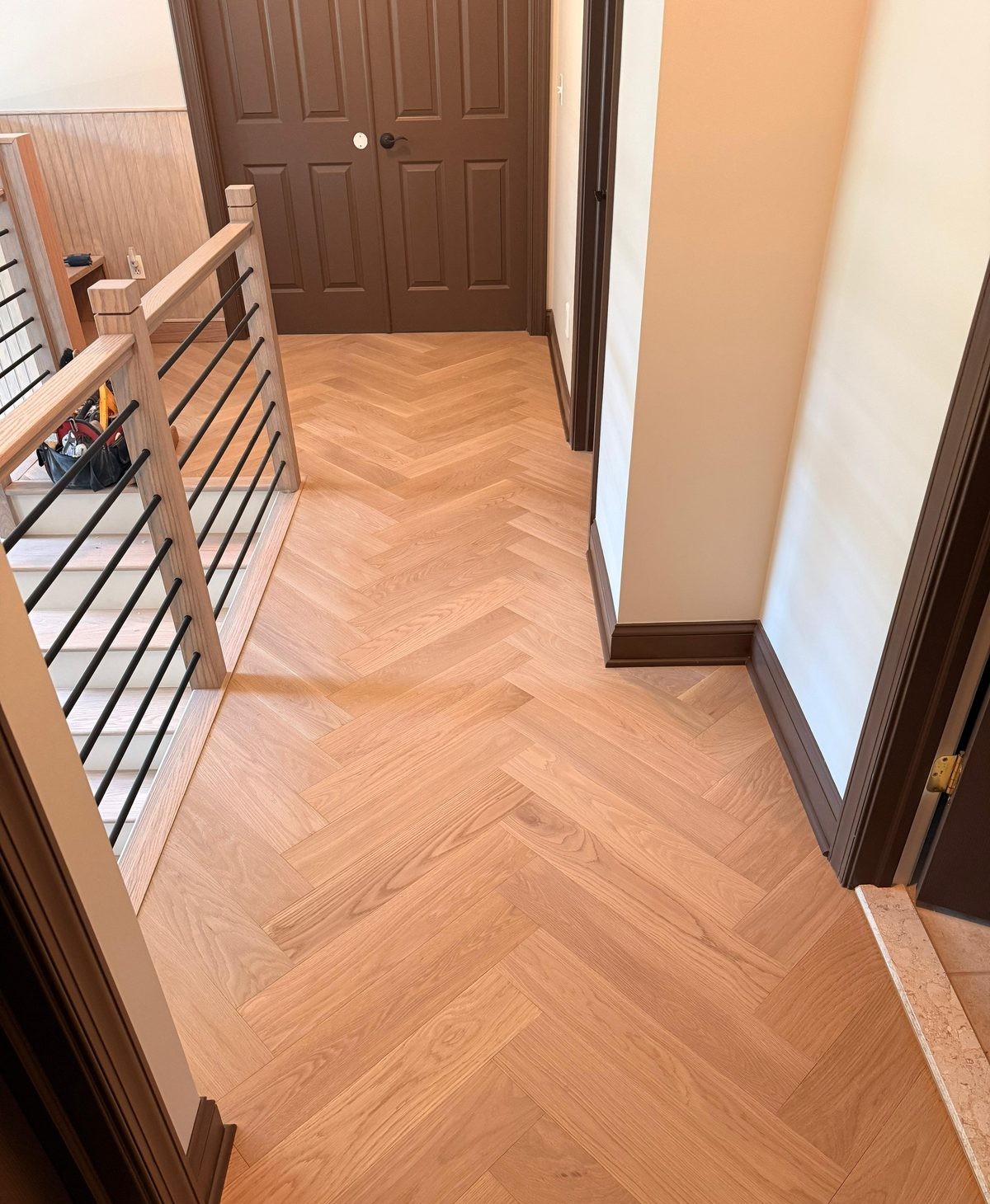Herringbone hardwood flooring in a hallway leading to a staircase.