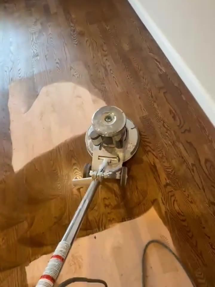 A floor sander working across a hardwood floor mid-refinish.