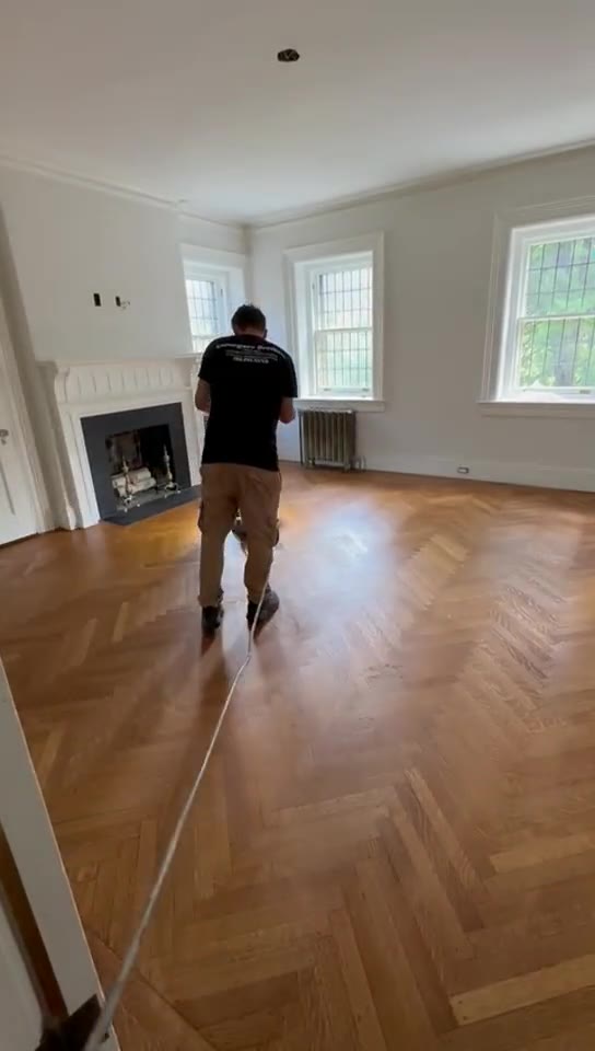 A technician sanding a large herringbone-pattern living room floor.