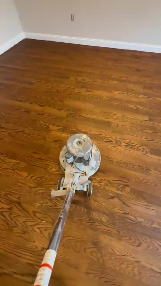 A drum sander working across a hardwood floor, revealing the natural wood tone.