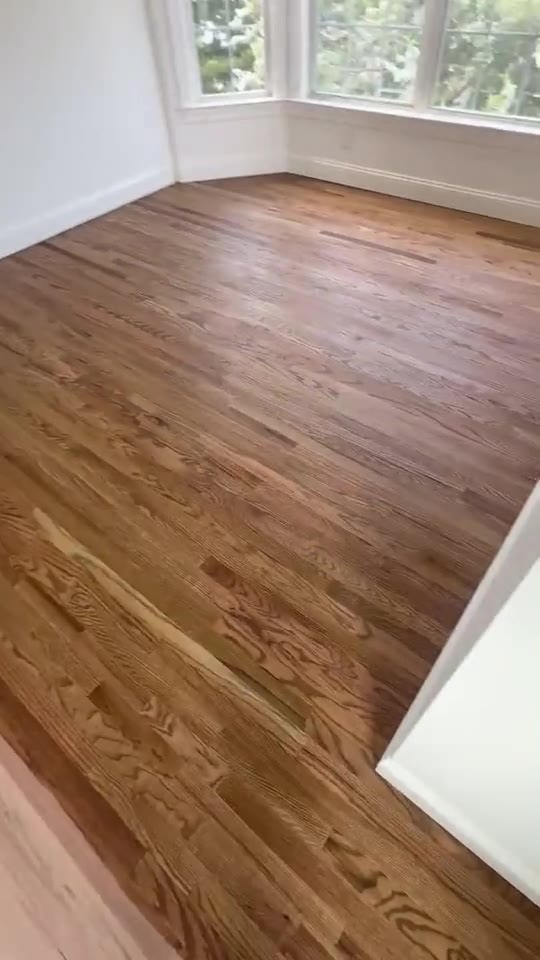 A richly stained hardwood floor in a sunlit bay window room.