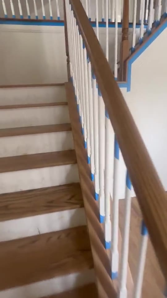 A staircase mid-refinish, with painter's tape protecting the risers and balusters.