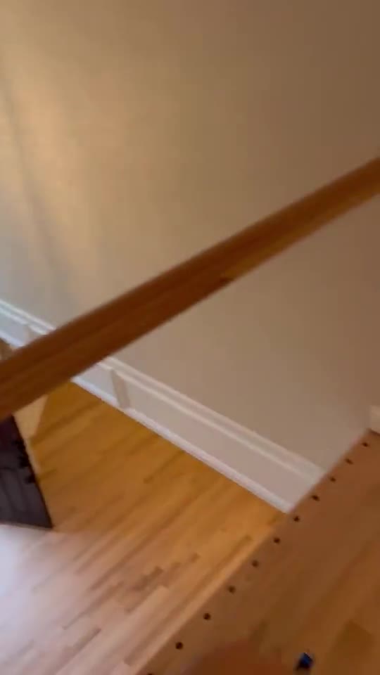 Moving along a stair railing toward a hardwood landing mid-refinish.