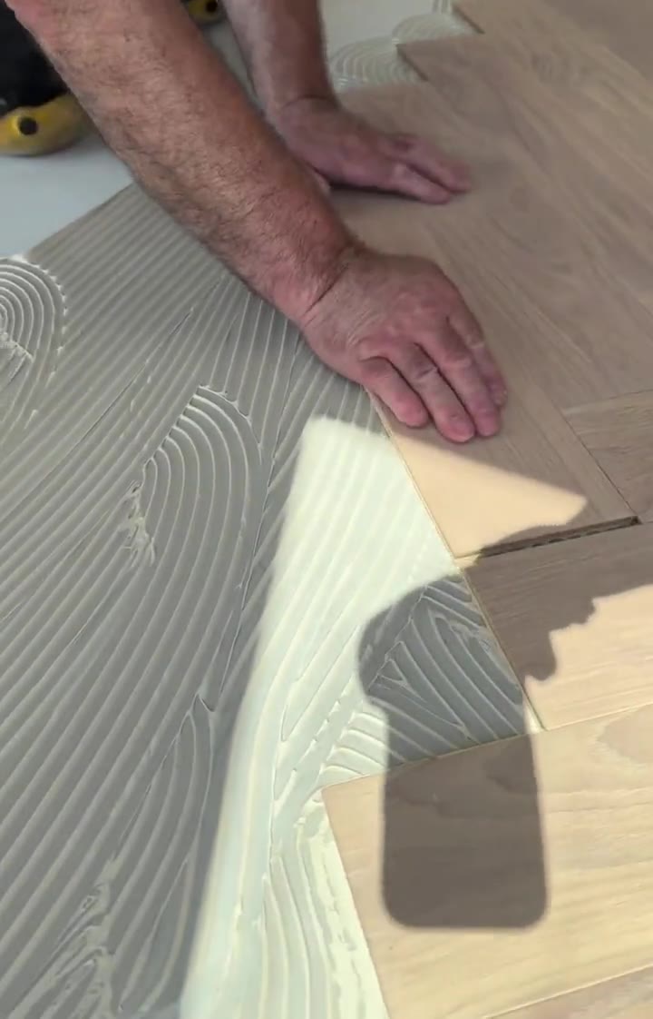 Setting a herringbone hardwood plank into fresh adhesive during installation.