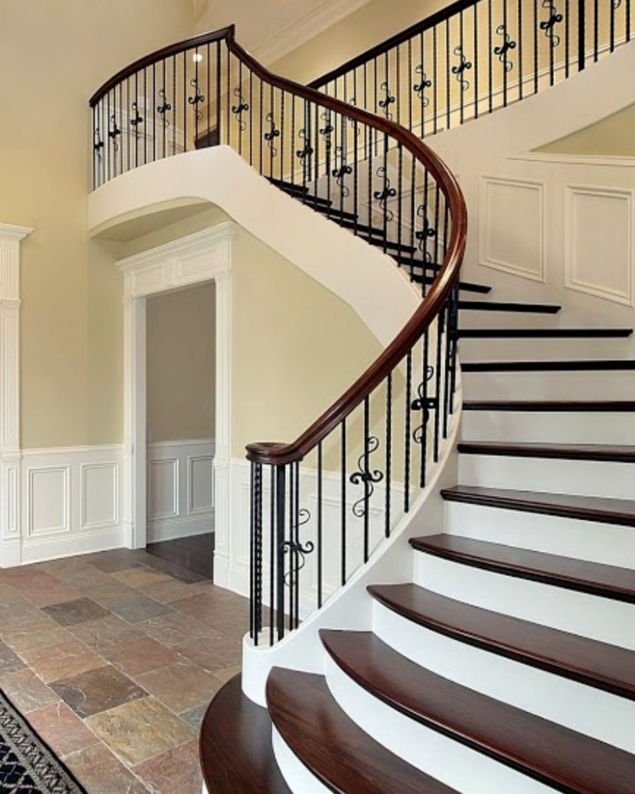 A curved staircase finished with dark wood treads and decorative iron balusters.